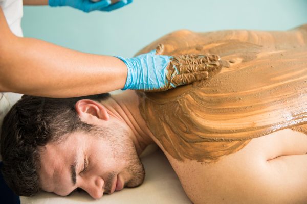 handsome-latin-young-man-getting-massage-mud-bath-during-his-visit-spa